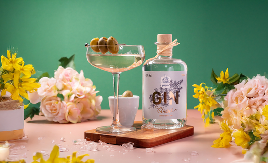 Martini-Gin-Cocktail mit Oliven neben einer Flasche „Dresdner Feingeist Classic Gin“, umgeben von Blumen – sommerlich, frisch und stilvoll inszeniert.