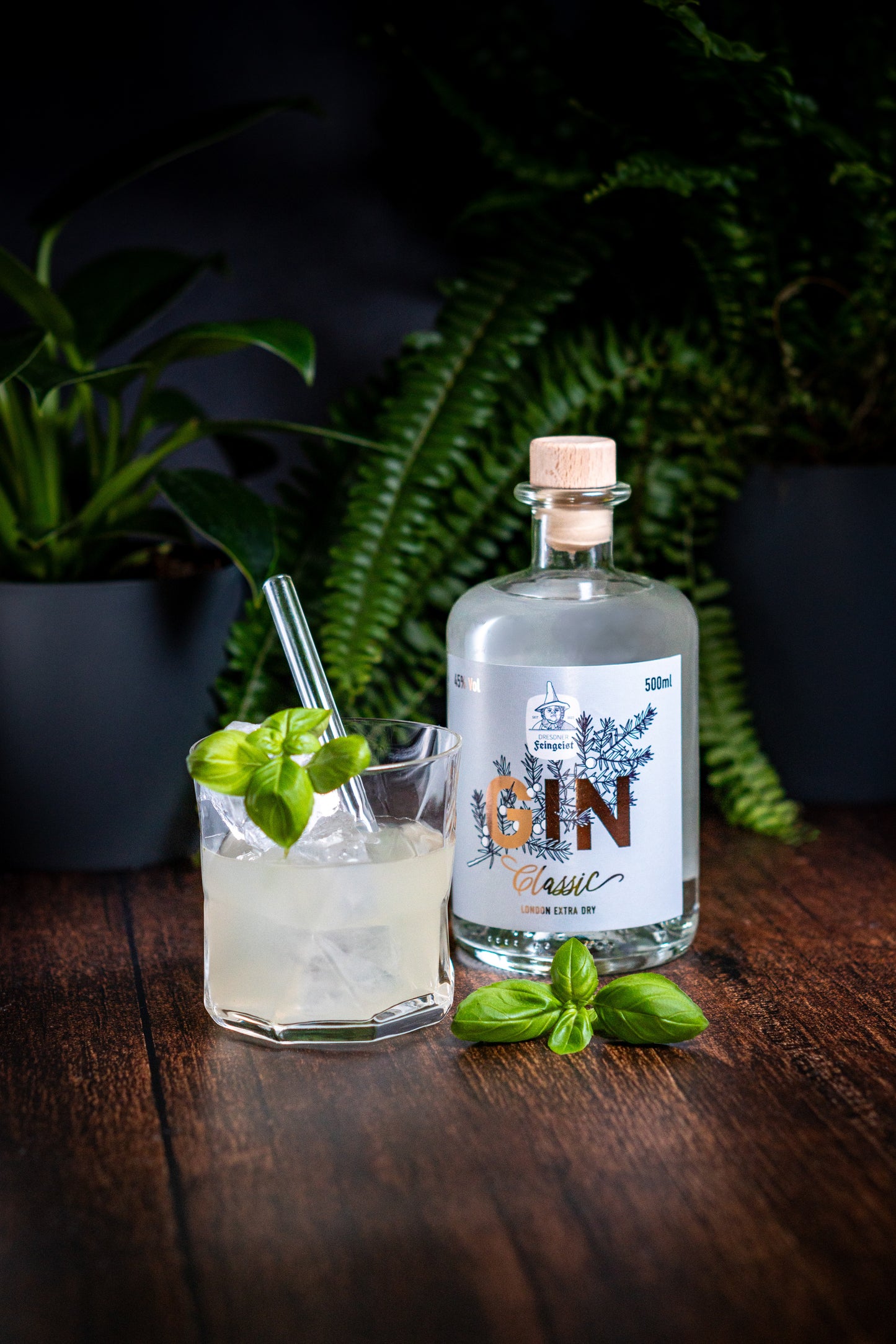 Eine Flasche Dresdner Feingeist Classic Gin neben einem gemixten Cocktail. Als Verzierung dient ein Basilikumstengel