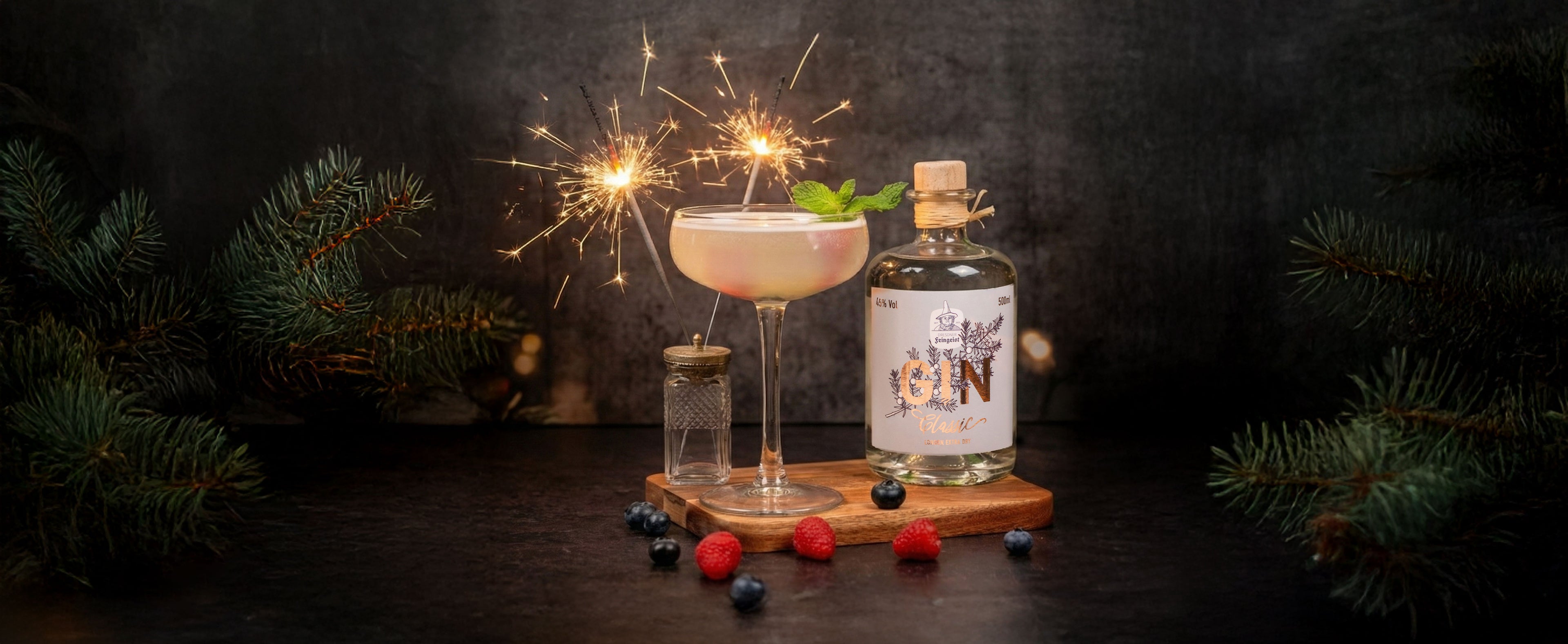 Eleganter Gin-Cocktail im Coupeglas mit Wunderkerzen als Garnitur, daneben eine Flasche Dresdner Feingeist GIN Classic auf Holzuntersetzer, umgeben von Beeren, Tannenzweigen und dunkler, festlicher Winterstimmung.